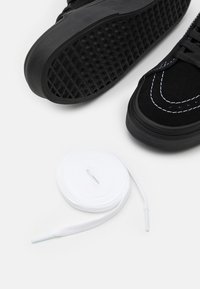 Czarne zamszowe sneakersy z białymi przeszyciami i gumowymi podeszwami, w zestawieniu z owiniętym białym sznurówką. Powierzchnia jest gładka, z wzorzystą podeszwą o przyczepności.