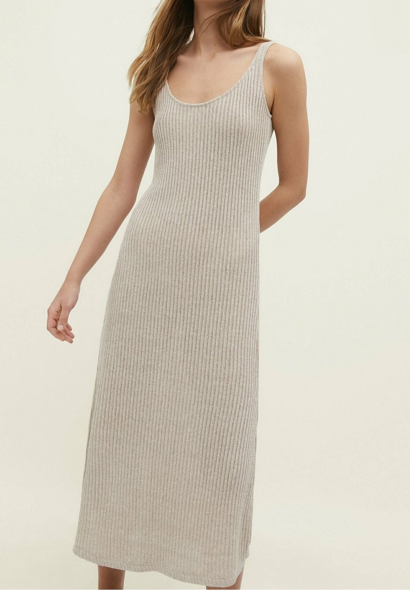 Robe en maille côtelée beige clair à encolure dégagée, conçue pour arriver au milieu du mollet. Présente des bretelles fines et une silhouette évasée.
