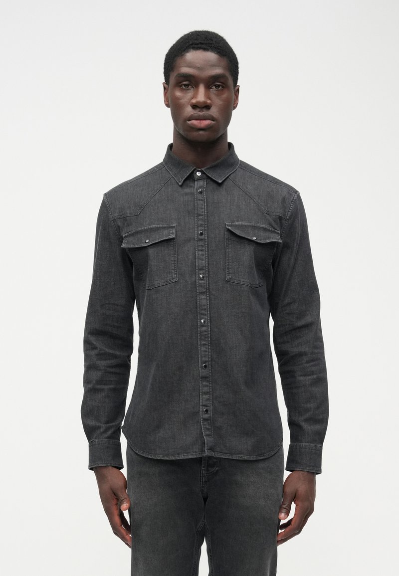 Men's black denim shirt with long sleeves, pointed collar, two chest pockets, button-up front, and subtle texture. Tailored fit.