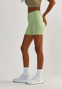 Jasnozielone sportowe szorty o wysokim stanie i gładkiej fakturze, z bocznymi kieszeniami i dopasowanym krojem. W zestawie z białymi trampkami.