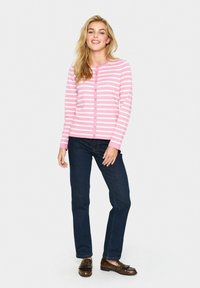 Cardigan rayé rose et blanc avec des boutons, à manches longues, porté sur un jean foncé et des mocassins. Design simple, texture douce.