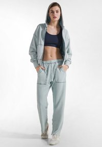 Lyseblåt træningssæt med lynlåshoodie og matchende joggingbukser. Har et cropped design, elastisk linning og to forlommer.