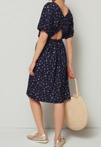 Námořnické květinové šaty s nabíranými rukávy, odhaleným zády a staženým pasem. V kombinaci se zlatými botami a kulatou slámovou taškou.