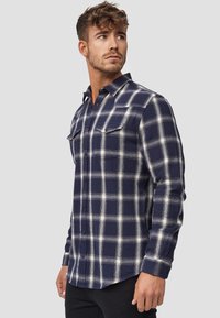 Navy and white plaid flannel shirt with button-up front, two chest pockets, and long sleeves. Soft fabric with a slightly textured finish.