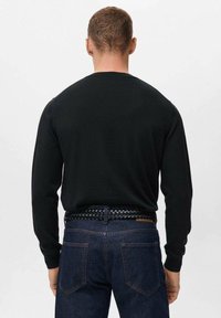 Pull noir à manches longues, coupe ajustée, avec un col rond et une texture lisse, porté avec un jean en denim foncé et une ceinture noire tressée.