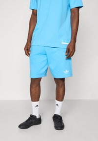 Light blue cotton t-shirt and matching shorts, featuring a white logo on the shorts, worn with white socks and black athletic shoes.