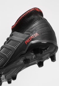 Black and red knitted ankle soccer cleat with molded studs and "Predator" branding on the heel.