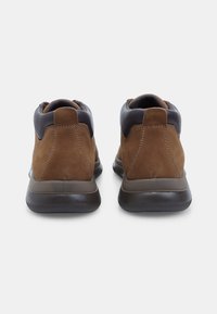 Botine din suede maro, cu accente din piele închisă, guler căptușit și un talpă din cauciuc texturat negru, având un design elegant și modern.
