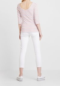 Top a maniche lunghe a righe rosa e bianche, con scollo a U sul retro. Abbinato a pantaloni attillati bianchi e sneakers bianche. Look semplice e casual.