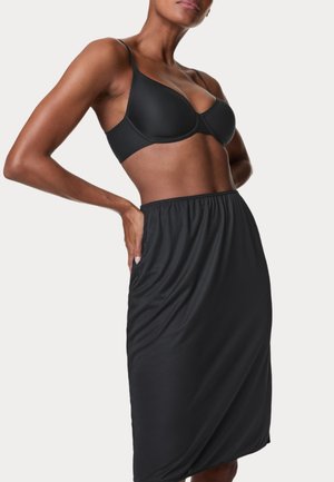 Reggiseno imbottito nero e gonna nera in tessuto morbido, lunga fino al ginocchio, con cintura elastica e tasche laterali. Texture liscia e design aderente.