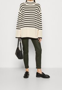 Czarny i biały pasiasty, oversize'owy sweter dzianinowy, oliwkowe, dopasowane spodnie, czarne loafersy i mała czarna torebka.
