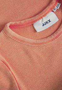 Maglietta a girocollo in tessuto a coste color corallo con superficie testurizzata, caratterizzata da un bordo leggermente più scuro e un'etichetta con la scritta "JJXX" in evidenza.