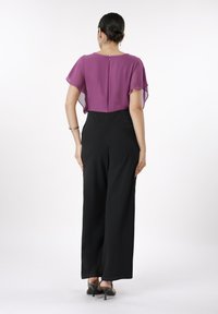 Svarte vide bukser kombinert med en lilla chiffon-topp med korte flagrende ermer og glidelås bak. Glatt stofftekstur.