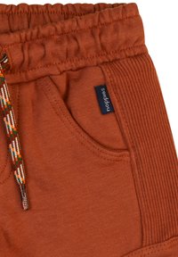 Brända orange bomullsshorts med elastiskt midjeband, dekorativt vävt snöre och sidoficka. Har en liten etikett med varumärket.