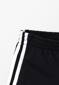 Pantalones cortos deportivos negros de tejido texturizado, con cintura ajustable mediante cordón y tres rayas verticales blancas a lo largo del costado.