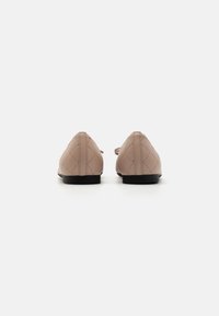 Ballerine in pelle beige con design trapuntato, punta affusolata e suola nera bassa. La parte posteriore presenta un dettaglio della cucitura accentuato.