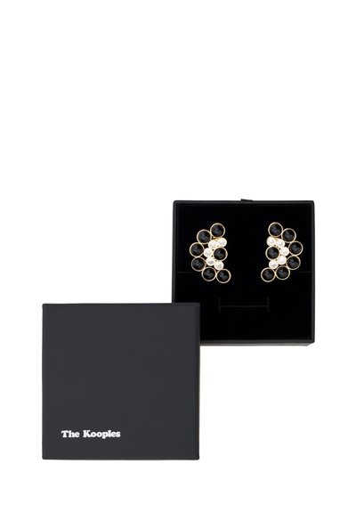 Gold- und schwarze Ohrstecker mit kreisförmigen Designs, die klare und schwarze Steine enthalten, präsentiert in einer schwarzen Box mit weißer Markenkennzeichnung.