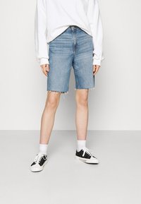 Jeanstunna i ljusblått med fransade kanter, kombinerat med en vit sweatshirt och svarta sneakers, med vita strumpor. Avslappnad passform och stil.