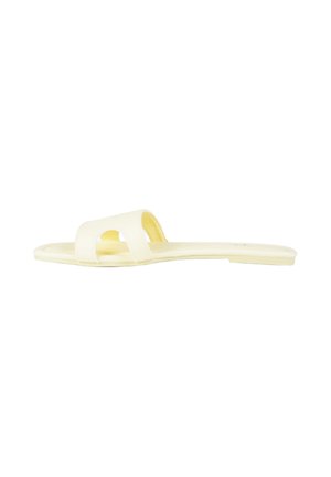 Sandalo piatto color crema con una larga fascia caratterizzata da un design traforato sulla parte superiore, mostrato su sfondo bianco.