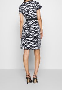 Robe à motifs noir et blanc avec des manches courtes, une taille cintrée et un tissu lisse. Présente une ceinture noire unie et une longueur au genou.