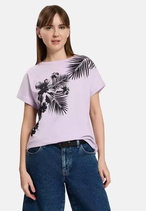 Lilac cotton t-shirt featuring black tropical plant print. Short sleeves, relaxed fit, paired with high-waisted blue denim jeans.