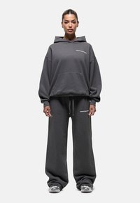 Grauer Kapuzenpullover und Jogginghose-Set, aus weichem Stoff gefertigt. Übergröße, mit Fronttaschen und minimalen Logoprints auf der Brust und den Hosen.