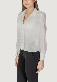 Blusa bianca a maniche lunghe con fronte plissettato, chiusura a bottoni e polsini in tinta unita a contrasto. Tessuto leggero e semitrasparente con una vestibilità sagomata.