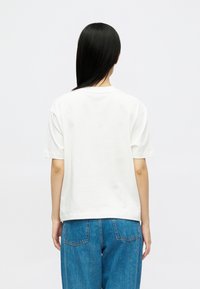 Λευκό βαμβακερό T-shirt με κοντό μανίκι, στρογγυλή λα�ιμόκοψη και χαλαρή εφαρμογή, το οποίο συνδυάζεται με μπλε τζην παντελόνι που διαθέτει εμφανείς πίσω τσέπες.