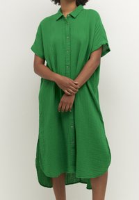 Vestito camicia verde, con bottoni, realizzato in tessuto leggero e testurizzato. Presenta un colletto, maniche corte e un orlo curvo. Design casual.