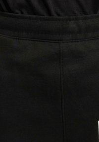 Fascia elastica nera con texture a coste. Il tessuto morbido presenta una minima lavorazione superficiale, con un taglio dritto e senza decorazioni visibili.