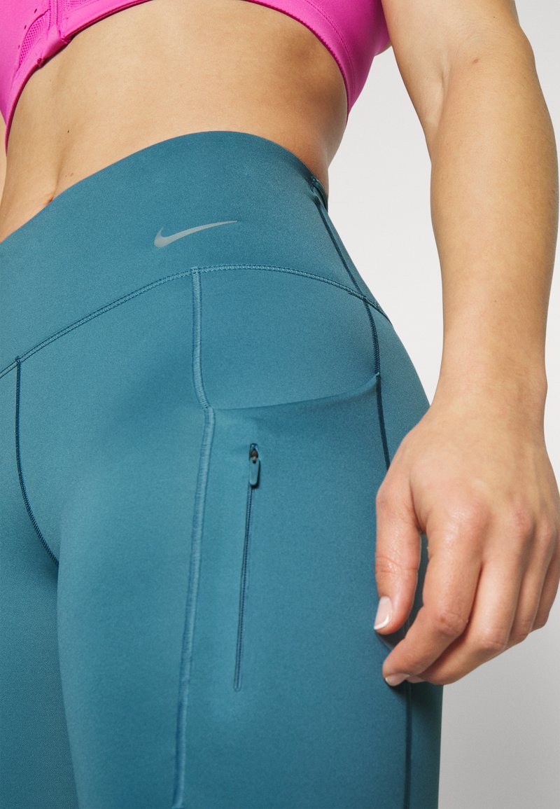 Türkise Leggings mit glatter Textur, ausgestattet mit einer seitlichen Reißverschlusstasche und kontrastierenden Nähten, hervorgehoben durch ein dezentes Nike-Logo in Grau.