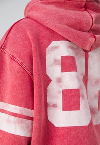 Sudadera roja con acabado desgastado, gran número blanco impreso "88" en la parte posterior, con rayas blancas en las mangas. Textura suave.