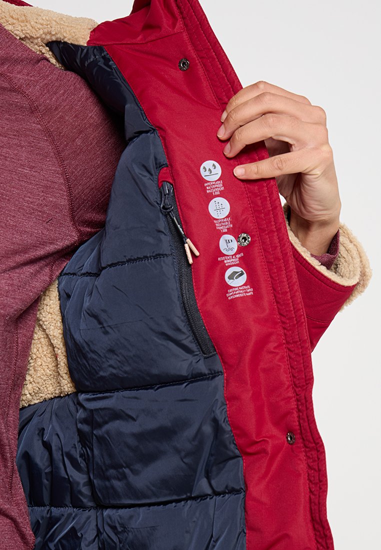 Hand, die eine offene rote Jacke hält und das marineblaue gesteppte Futter zeigt, mit Symbolen für Funktionen wie Leitfähigkeit, wasserdicht, atmungsaktiv und winddicht auf dem inneren Klappenteil.