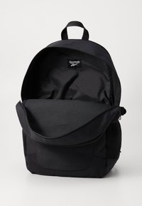 Čierny batoh s horným zipsom, logo Reebok, dizajn s dvoma priehradkami, sieťované bočné vrecká, odolná tkanina a polstrované popruhy pre pohodlie.