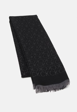 Écharpe noire avec motif de logo "CK" gris et bords frangés gris, pliée sur un fond blanc.