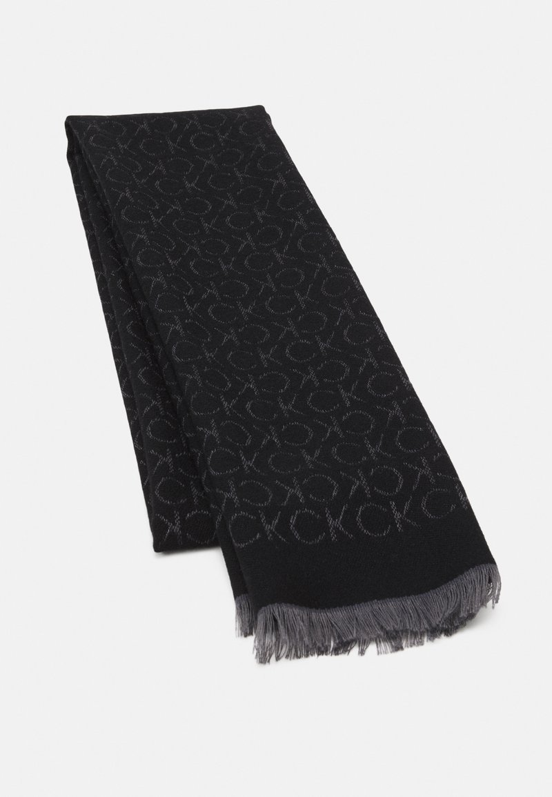 Écharpe noire avec motif de logo "CK" gris et bords frangés gris, pliée sur un fond blanc.