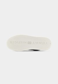 Λευκή λαστιχένια σόλα αθλητικού παπουτσιού με υφή αντιολισθητικότητας και το ανάποδο κείμενο "TOMMY HILFIGER" αποτυπωμένο στον πάτο.