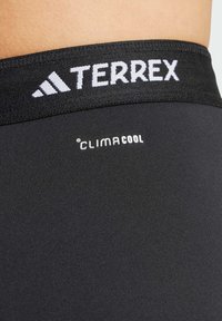 Czarne legginsy sportowe o gładkiej teksturze, z szerokim elastycznym pasem w odblaskowym logo "TERREX" oraz metką "CLIMACOOL".