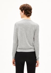 Grijze gebreide trui met lange mouwen, ronde halslijn en ribbelzoom. Glad oppervlak; gedragen met zwarte broeken. Achteraanzicht getoond.