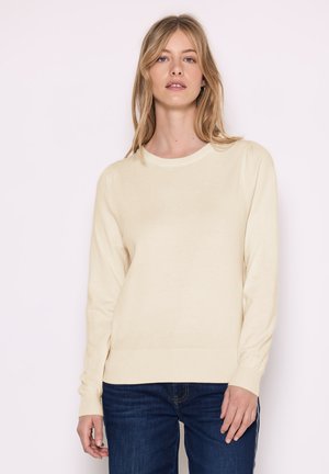 Cremefarvet sweater lavet af blødt stof, med rund halsudskæring, lange ærmer og ribbede manchetter og kant. Båret med mørkeblå jeans.
