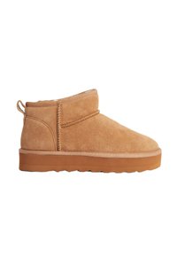 Bottine en suède beige avec un bout arrondi, un talon légèrement surélevé et un détail de couture décoratif sur le côté. Semelle en caoutchouc avec traction.