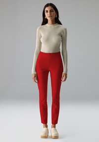 Geribbeld crèmekleurig langemouwen top, aansluitende rode broek en lichte houten klompen. Eenvoudig ontwerp met een gladde textuur en een gepaste pasvorm.