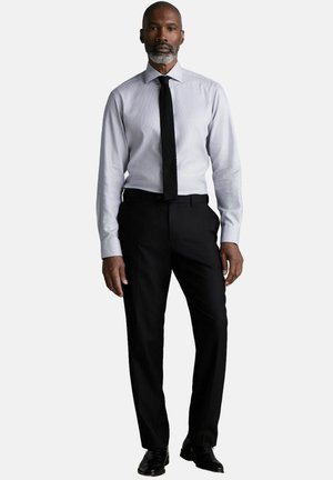 Conjunto formal que incluye una camisa de un gris claro con patrón, una corbata negra y pantalones negros. Se evidencian texturas suaves y un corte a medida.
