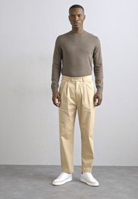 Brun langermet skjorte, beige plissert bukser og hvite joggesko. Antrekket har en avslappet passform og glatte teksturer.