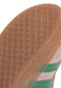 Semelle en caoutchouc avec un motif texturé comportant des formes d'étoiles ; couleur marron pâle. Dessus rose pâle adjacent avec des accents de bandes vertes.