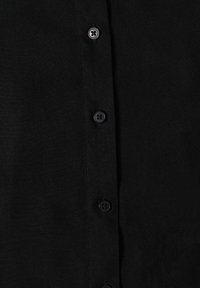 Gros plan sur un tissu noir avec quatre boutons noirs cousus verticalement le long d'une patte de boutonnage.