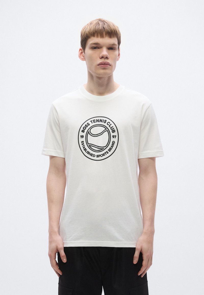 Balti medvilniniai marškinėliai su apvaliu juodu tenisraketės spaudiniu ir užrašu „BOSS TENNIS CLUB 1967 ĮKURTA SPORTO PREKĖS ŽENKLAS".