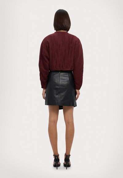 Burgundijas krāsas īsā džemperis ar teksturētu audumu, savienots ar melnu ādas mini svārku, kuram ir aizmugures rāvējslēdzis un gluda virsma.