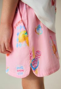 Hand van kind rust naast een roze rok met kleurrijke zomerse prints, waaronder citroenen, hartjes en tekst met de woorden "Sunshine Club."