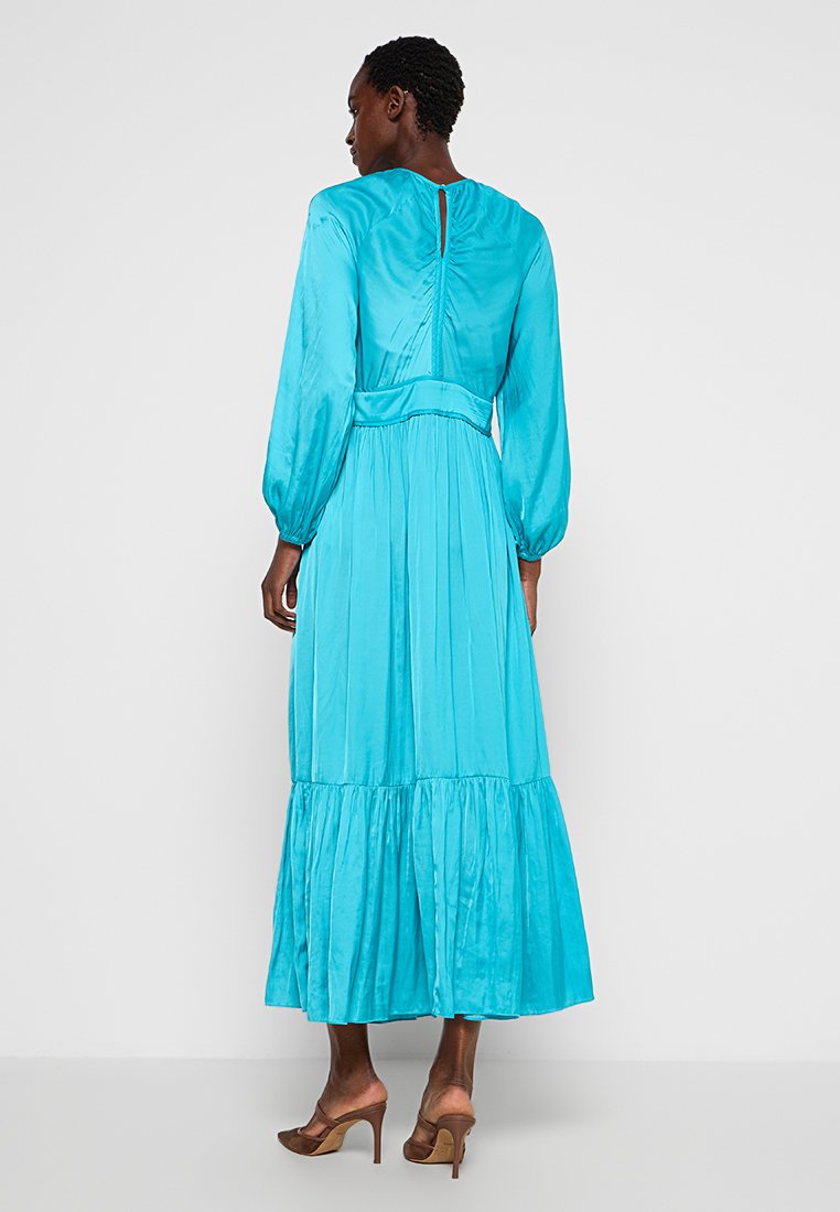 Ein langes, ärmelloses Kleid aus lebhaftem türkisfarbenem Satin, das einen gerafften Rücken, breite Ärmel und einen gestuften Volant-Saum aufweist.